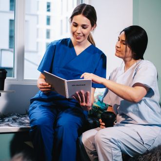 Zwei Krankenpflegerinnen zeigen auf einen Flyer von ilomed