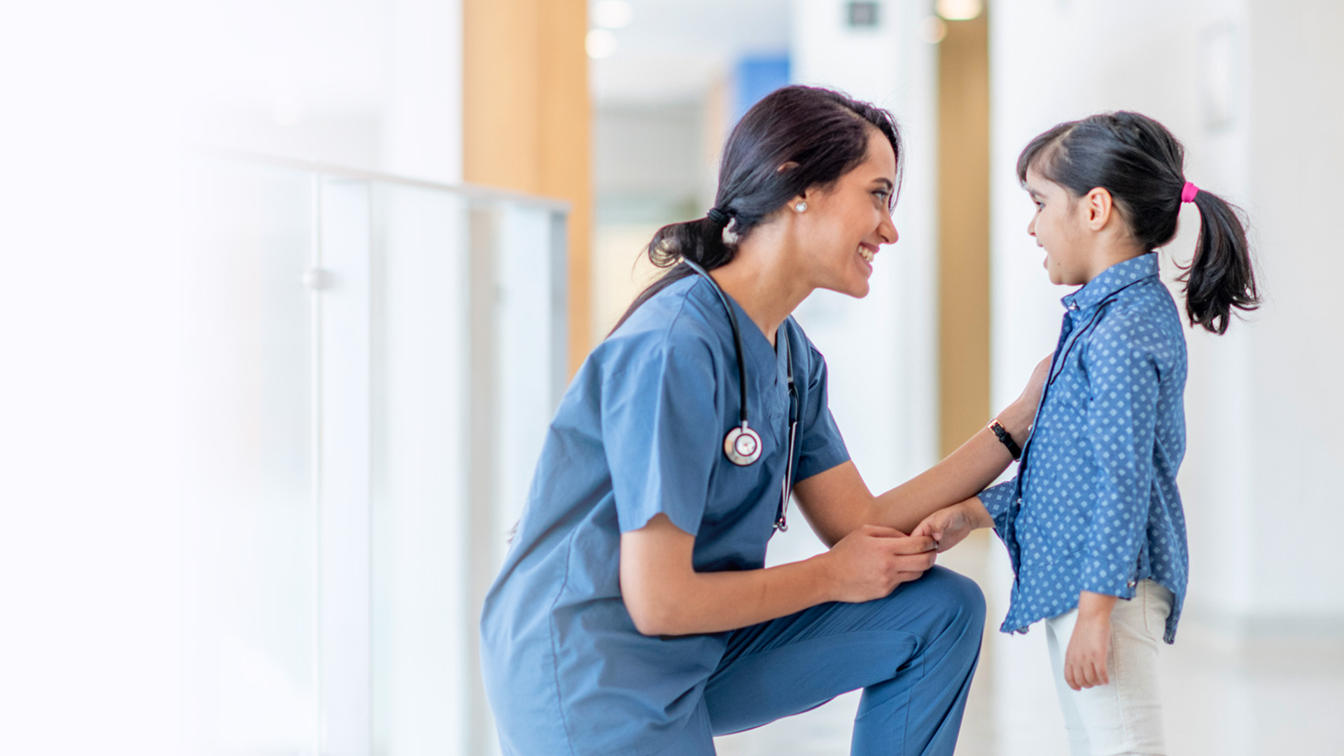 Eine Kinderkrankenpflegerin von ilomed kniet vor einem Mädchen